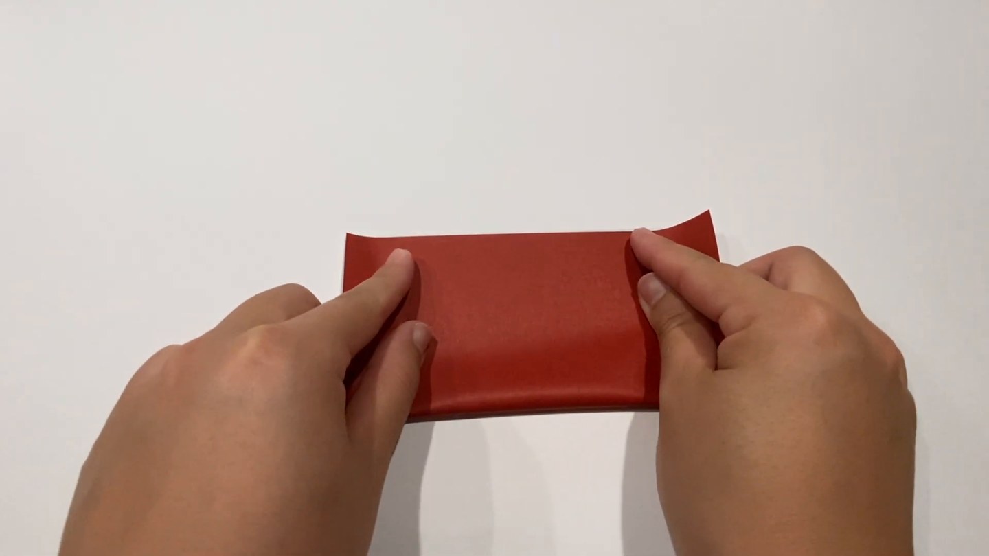 赤い面を上にした折り紙を半分に折っているところ