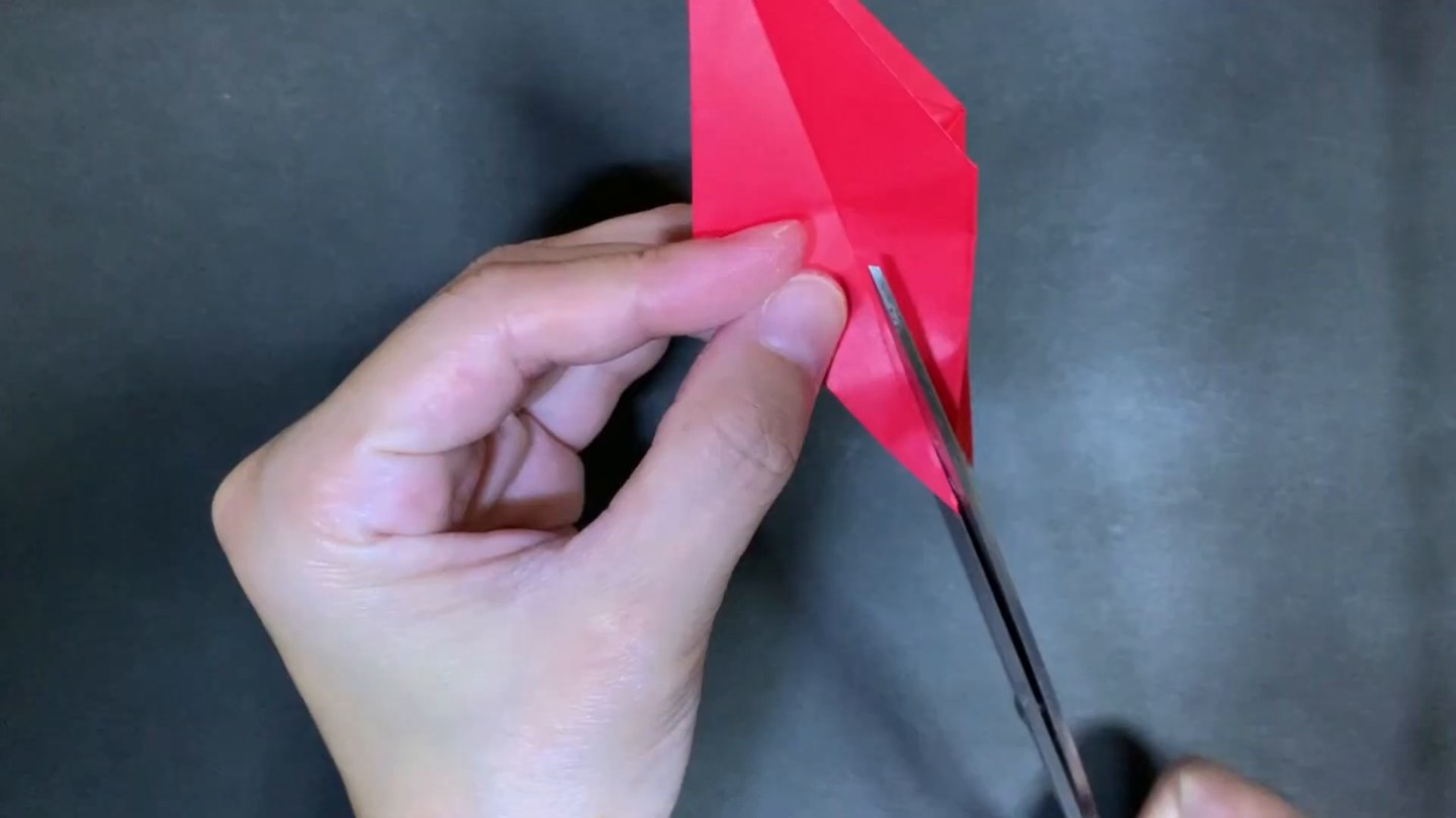 折りたたんだ赤い折り紙の先にはさみが入り、切り込みを入れている