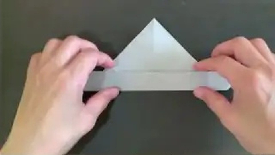 白い折り紙の上に三角の形があり、その下に細い帯が横に出ているところを両手で持っている