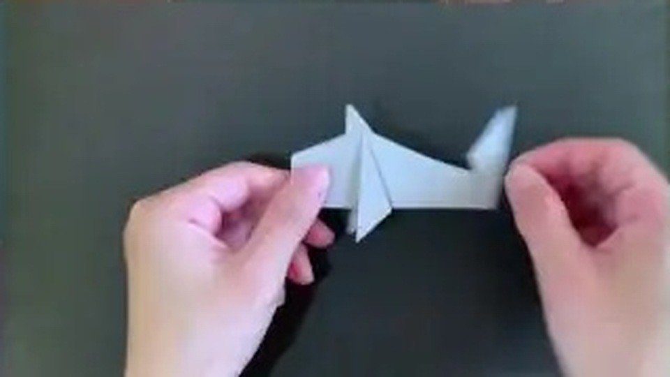 左に三角の頭、右にとがった尾びれができた、顔を描く前の白いサメの折り紙を両手で持っている