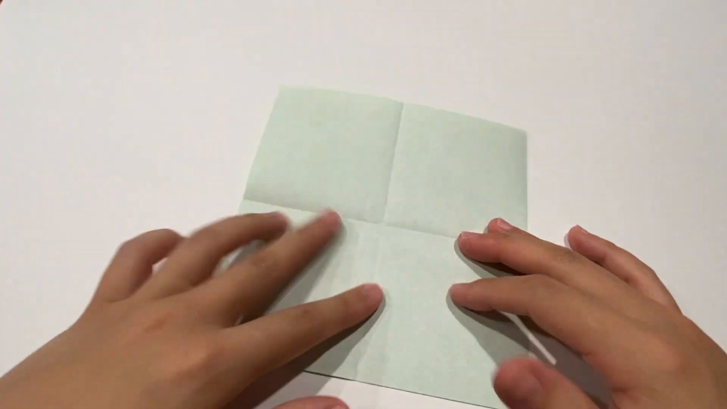 白い面に縦と横の十字の折り目がついた正方形の折り紙を、両手で押さえている