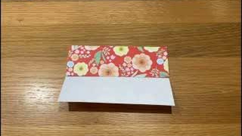 上半分が赤い花柄で下半分が白い面の、横長に折った帯を机に置いているところ