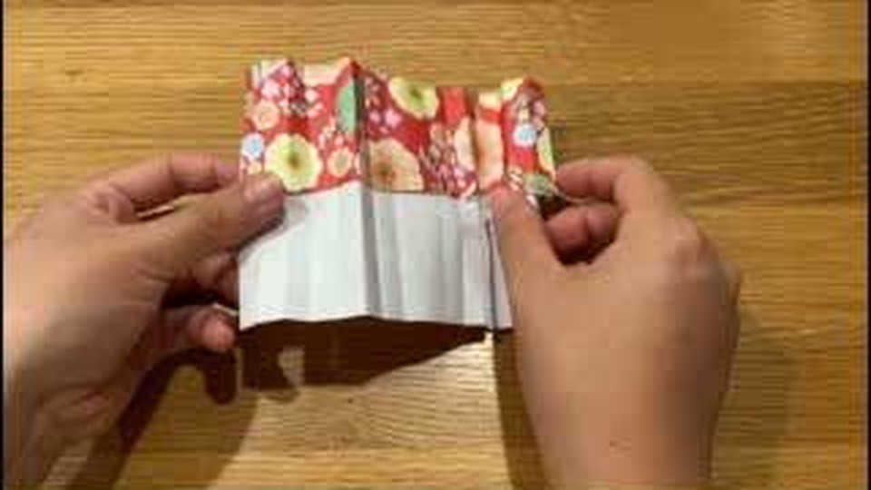 赤い花柄と白い面にじゃばらの折り目がついた紙を、両手で広げて持っているところ