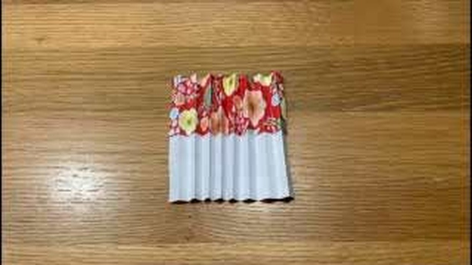 上が赤い花柄で下が白い、折り目のそろったじゃばらの紙を机に置いているところ