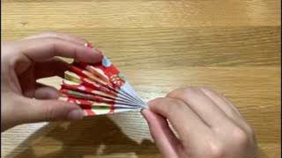 根元をひもでとめた赤い花柄の紙を、両手で扇形に開いているところ