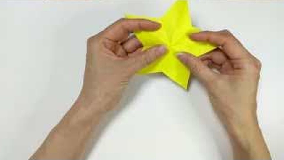 切った黄色い紙を開き、5つの角のある星の形が見えてきている
