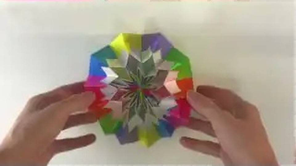 輪の形に組み上がった、色とりどりの花のような折り紙を両手で支えている